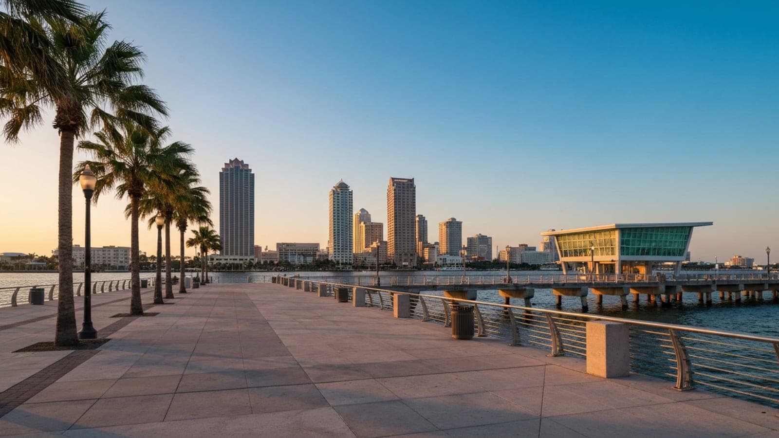 Editorial photograph of the St. Petersburg Pier District at golden hour with a waterfront pier extending into Tampa Bay and the downtown skyline behind.