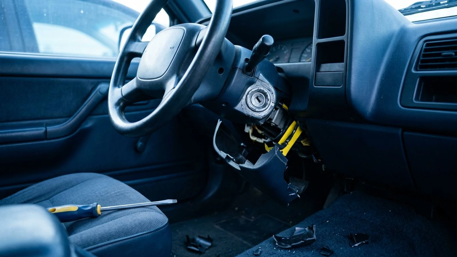 A car steering column with its plastic cover broken away and the ignition lock cylinder exposed, seen from the driver seat